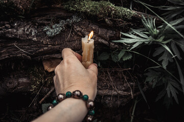 burning candles and a womans hand with a bracelet on a dark natural background. pagan wiccan, slavic traditions. Witchcraft, esoteric spiritual ritual for mabon, samhain. autumn equinox festival - obrazy, fototapety, plakaty