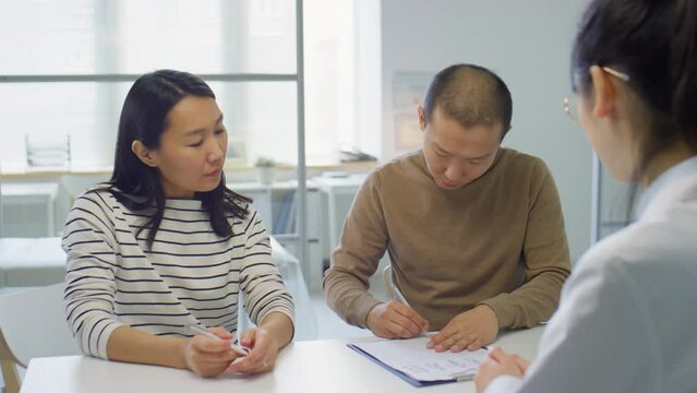 Asian family couple signing contract during consultation with female doctor in pregnancy clinic