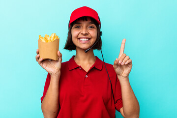 Young mixed race woman fast food restaurant worker holding fries isolated on blue background showing number one with finger.