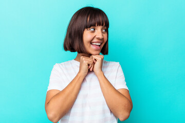 Young mixed race woman isolated on blue background keeps hands under chin, is looking happily aside.