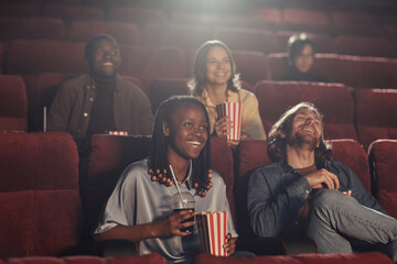 Happy friends eating popcorn with soda and enjoying the movie in cinema