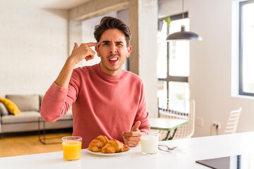 Fototapeta na wymiar Young mixed race man having breakfast in a kitchen on the morning showing a disappointment gesture with forefinger.