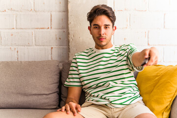 Young mixed race man watching TV sitting on the sofa in his house