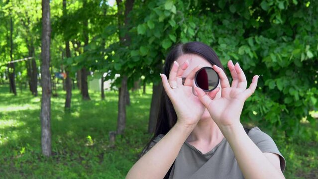 The girl holds an ND filter in her hands and looks through it with one eye and slowly twists it, the filter turns black