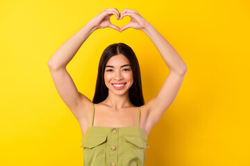 Fototapeta na wymiar Photo of lovely cute malaysian girl hands fingers show heart gesture above head toothy smile isolated on yellow color background