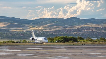 White business jet with turbofan engines on the airport with attractive panoramic mountain...