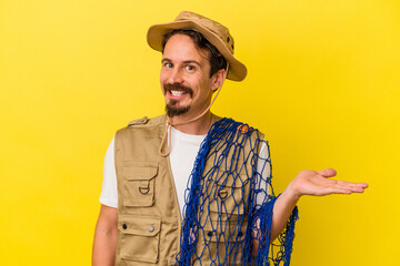 Young caucasian fisherman holding net isolated on yellow background showing a copy space on a palm...