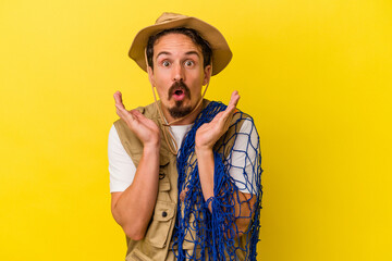 Young caucasian fisherman holding net isolated on yellow background surprised and shocked.