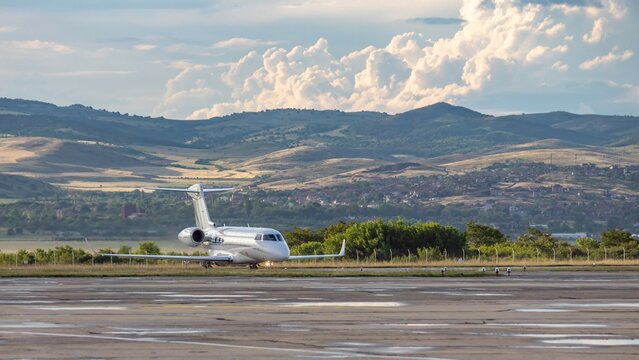 White business jet with turbofan engines on the airport with attractive panoramic mountain landscape and cloudy sky. Modern technology in fast transportation, business travel and tourism, aviation.