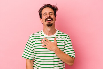 Young caucasian man isolated on pink background laughs out loudly keeping hand on chest.