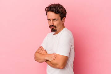 Young caucasian man isolated on pink background frowning face in displeasure, keeps arms folded.