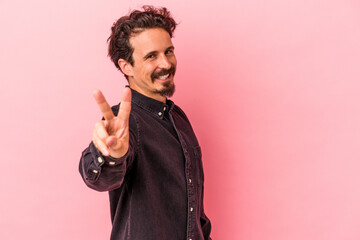 Young caucasian man isolated on pink background joyful and carefree showing a peace symbol with fingers.