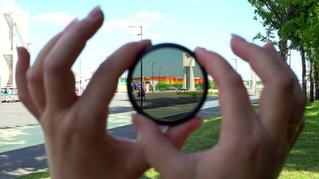 View of a beautiful multi-colored building through round tinted glass. Women's hands twist the ND filter and it becomes transparent