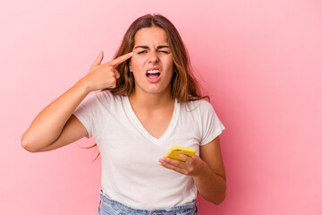 Young caucasian woman using mobile phone isolated on pink background  showing a disappointment gesture with forefinger.