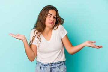 Young caucasian woman isolated on blue background  doubting and shrugging shoulders in questioning...