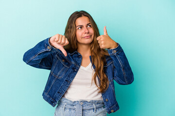 Young caucasian woman isolated on blue background  showing thumbs up and thumbs down, difficult...