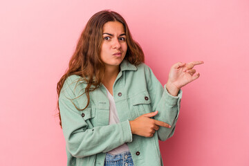 Young caucasian woman isolated on pink background  shocked pointing with index fingers to a copy space.