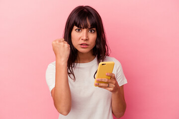 Young caucasian woman holding a mobile phone isolated on pink background showing fist to camera, aggressive facial expression.