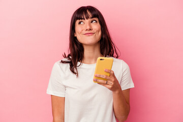 Young caucasian woman holding a mobile phone isolated on pink background dreaming of achieving...