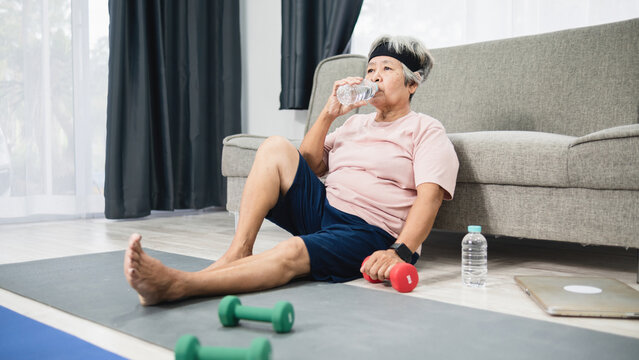 Home workout concept, Asian elderly woman Drinking water after exercise.