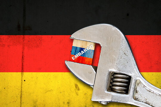 Embargo. Word on a wooden block in the colors of the Russian flag. Clamped wrench. Against the background of the flag of Garmany. Business. Politics.