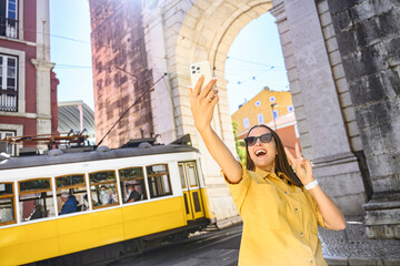 Overjoyed happy foreign woman tourist taking selfie with famous yellow tram, walking in old town of...