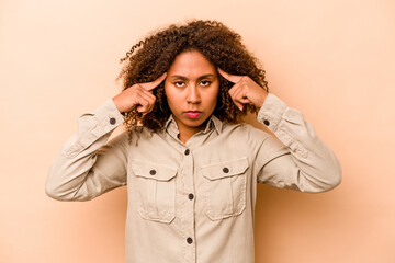 Young African American woman isolated on beige background focused on a task, keeping forefingers pointing head.