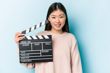 Young asian woman holding clapperboard isolated on blue background laughing and having fun.