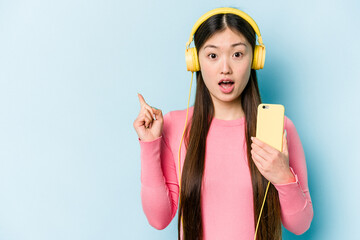 Young asian woman listening to music isolated on blue background pointing to the side