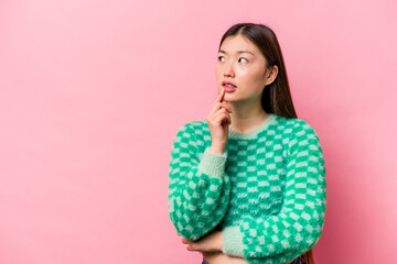 Young Chinese woman isolated on pink background looking sideways with doubtful and skeptical expression.
