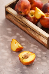 Many whole and cut in slices peaches in wooden basket on purple background