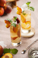 Two glasses with refreshing summer cocktail with ice cubes, peach slices and fresh mint on pale purple background