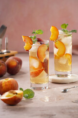 Two glasses with refreshing summer cocktail with ice cubes, peach slices and fresh mint on pale purple background
