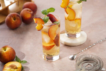 Two glasses with refreshing summer cocktail with ice cubes, peach slices and fresh mint on pale purple background
