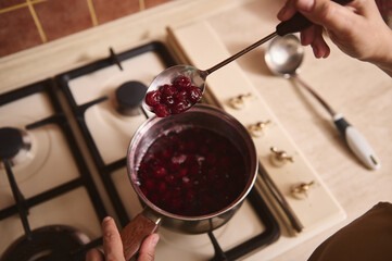 Top view of a chef confectioner's hands stirring boiling cherry berry jam with sugar while cooking...