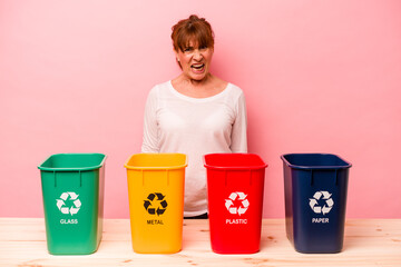 Middle age woman recycling isolated on pink background screaming very angry and aggressive.