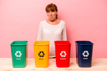 Middle age woman recycling isolated on pink background shrugs shoulders and open eyes confused.