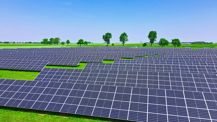 Solar panels battery in green field against blue sky, aerial view. Photovoltaic modules for renewable energy. Concept of clean, sustainable, alternative energy