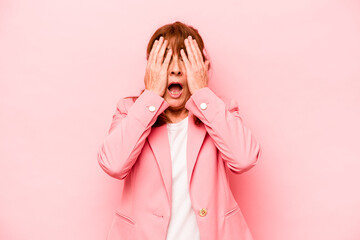 Middle age caucasian woman isolated on pink background having fun covering half of face with palm.