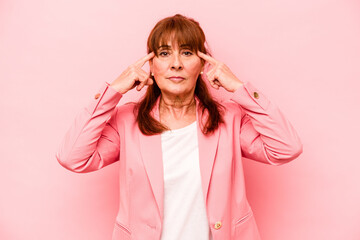 Middle age caucasian woman isolated on pink background focused on a task, keeping forefingers pointing head.