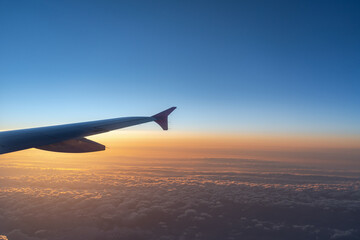 Up in the air, view of aircraft wing silhouette with dark blue sky horizon and cloud background in sun rise or sunset time from airplane window.