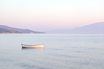 Naklejka premium Tranquil pink sunrise or sunset over glowing sea ocean calm waters. Lonely boat. Sun low over horizon. water landscape. Copy space. Travel vacation destination scenics