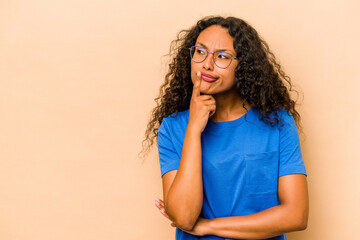 Young hispanic woman isolated on beige background looking sideways with doubtful and skeptical expression. - obrazy, fototapety, plakaty
