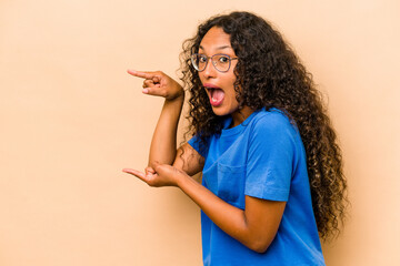 Young hispanic woman isolated on beige background excited pointing with forefingers away.