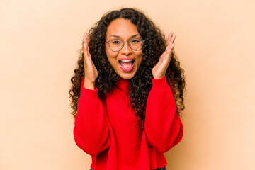 Young hispanic woman isolated on beige background laughs out loudly keeping hand on chest.