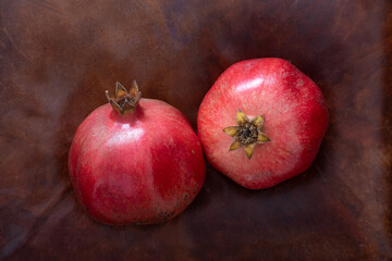 Two red pomegranate sweet fruit on a brown leather  background. Symbol of healthy nutrition