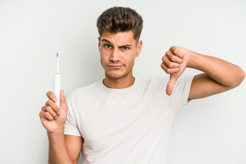 Young caucasian man holding a electric toothbrush isolated on white background showing a dislike...