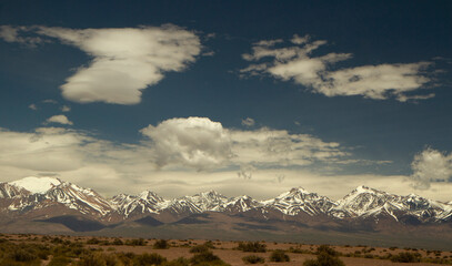 Alpine landscape. Panoramic view of the Andes cordillera mountains with snowy peaks, under a beautiful blue sky with clouds.