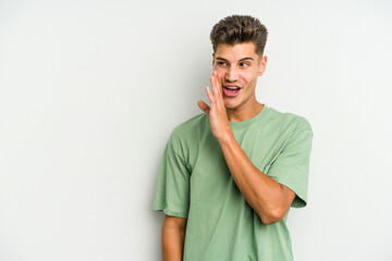 Young caucasian man isolated on white background is saying a secret hot braking news and looking aside