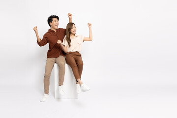 Attractive young Asian businessman and businesswoman sitting on white box and hands up raised arms...